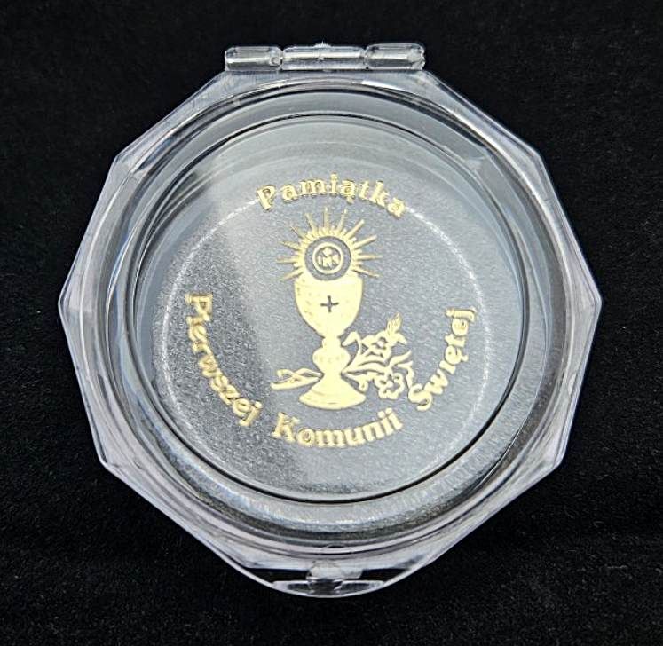 Przezroczyste, ośmiokątne pudełko na pamiątkę Pierwszej Komunii Świętej z nadrukiem złotego kielicha i hostii, widoczną białą pianką PU w środku, leżące na ciemnym tle.