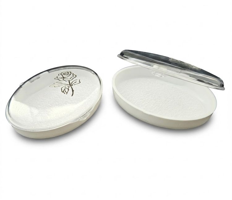 Białe owalne pudełko na różaniec z przezroczystym wieczkiem i złotym nadrukiem róży.