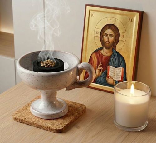 Ręczna kadzielniczka ceramiczna dymiąca przed ikoną Jezusa Pantokratora, węgielek trybularzowy z kadzidłem żywicznym.