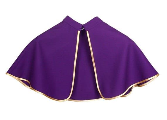 Fioletowa pelerynka ministrancka ze złotą lamówką, zapinana pod szyją, leżąca na białym tle e-religijne.pl